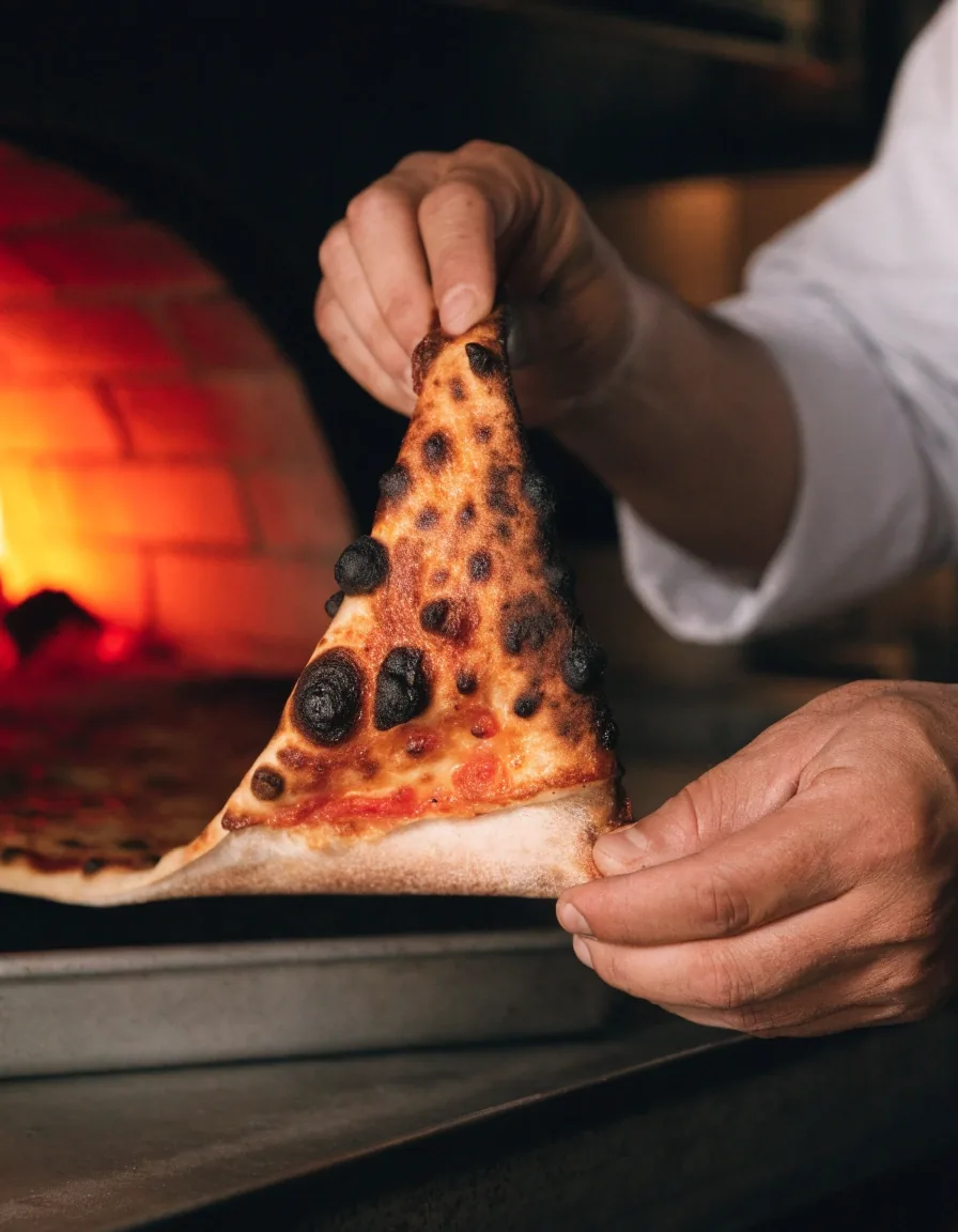 Thin coal-fired pizza lifted from the tray showing a crisp base